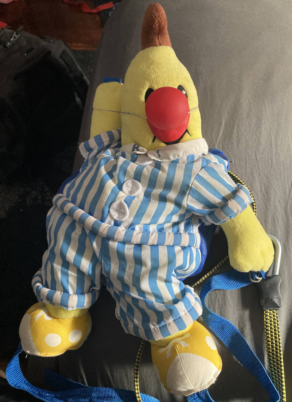 B1 Bananas in Pyjamas plushy bag wearing red clown nose. Sprawled on bed.