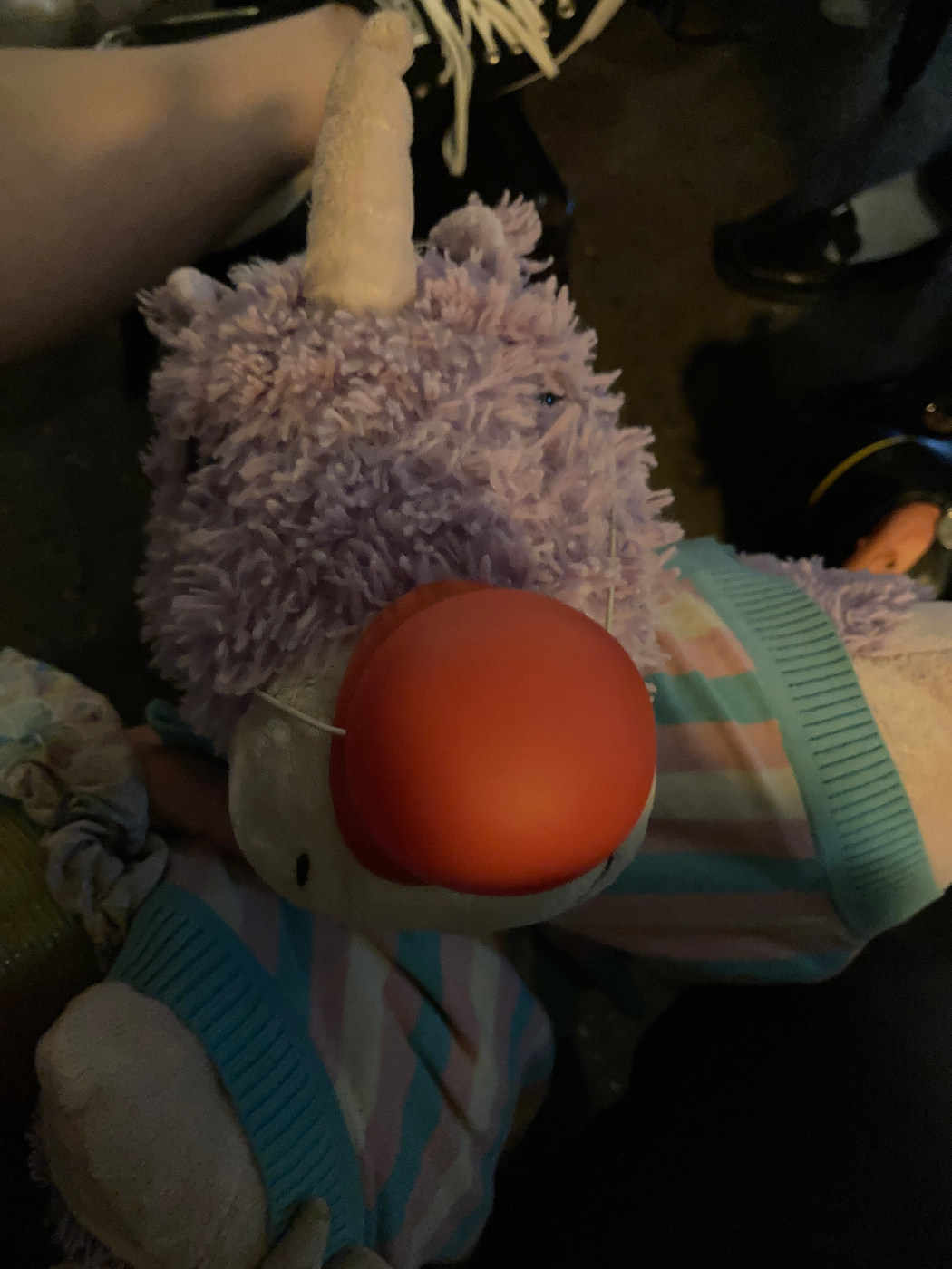 Purple unicorn pillow pet. Red clown nose, wearing trans flag sweater.