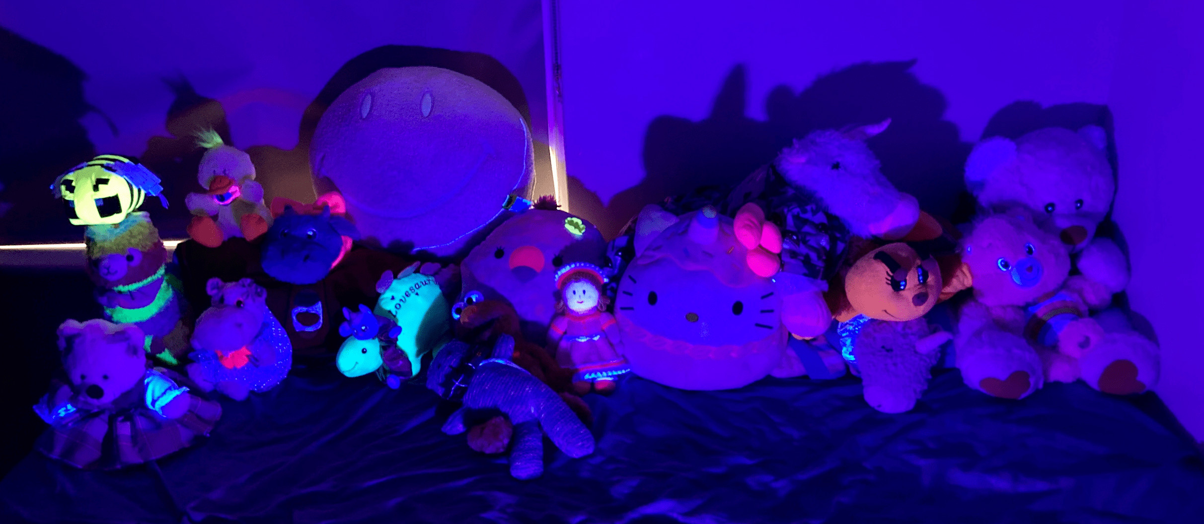 All of SlinkyFam's plushies laid out on bed in darkness UV