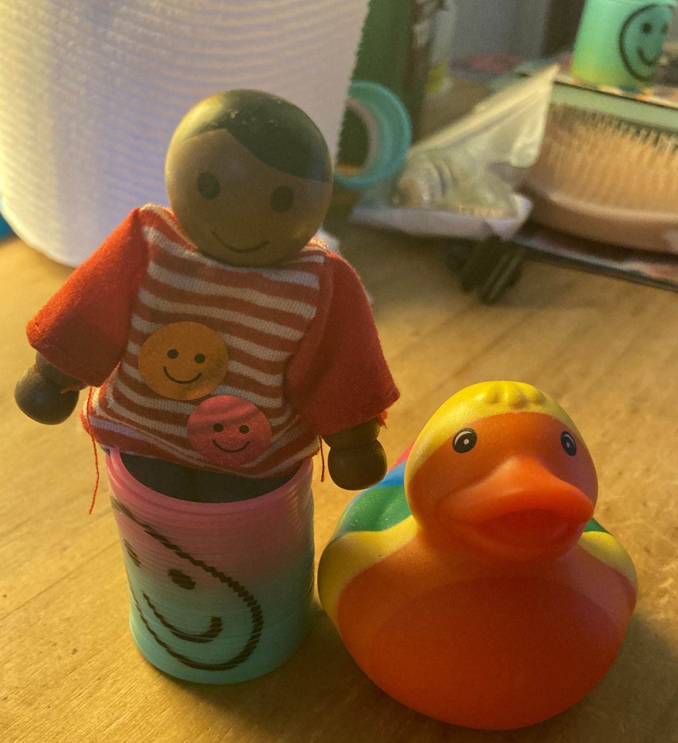 Mini wooden figure, striped shirt, smiling. Rainbow ducky and mini slinky.