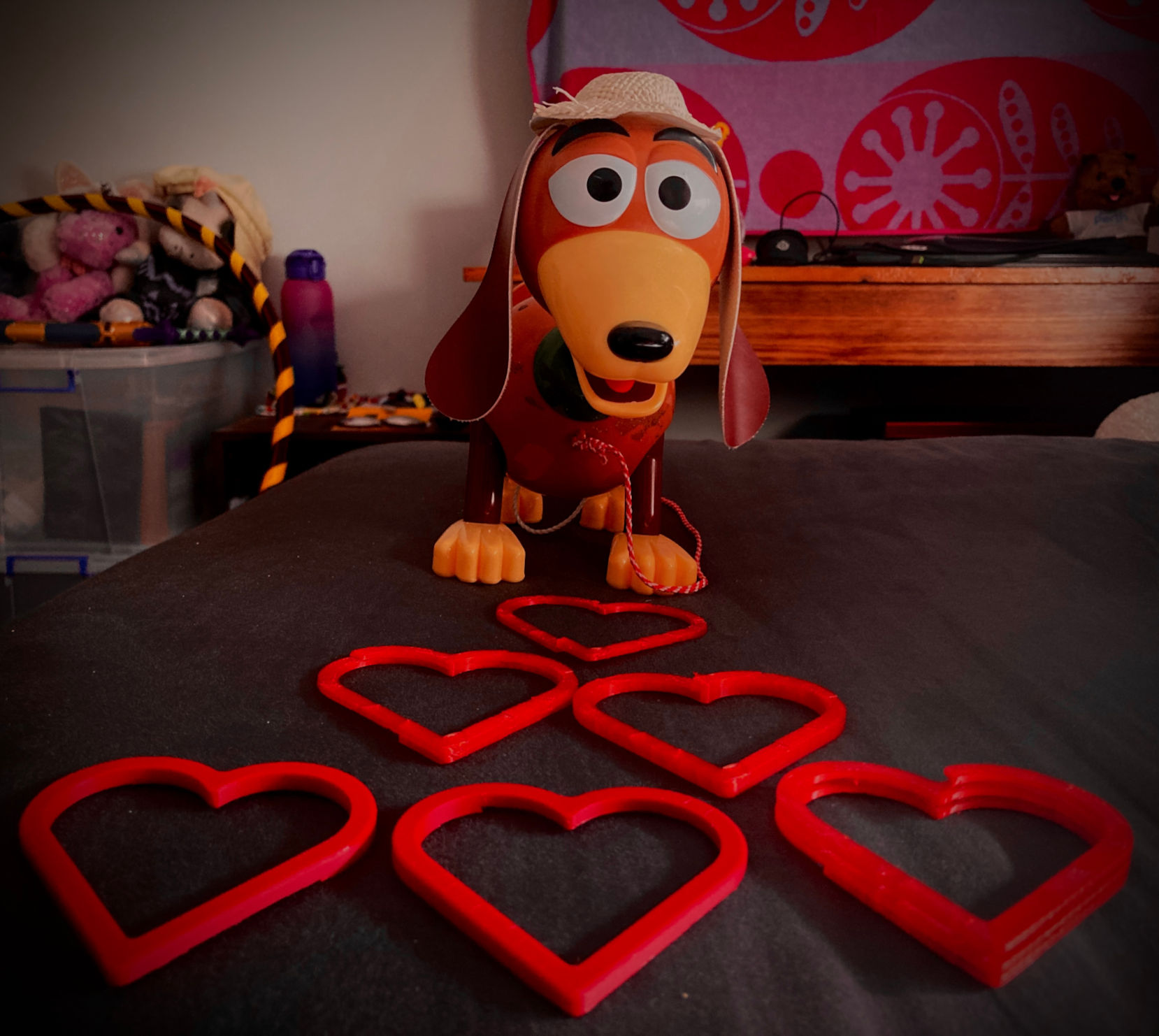Slinky Dog positioned on bed with six red hollow love hearts.