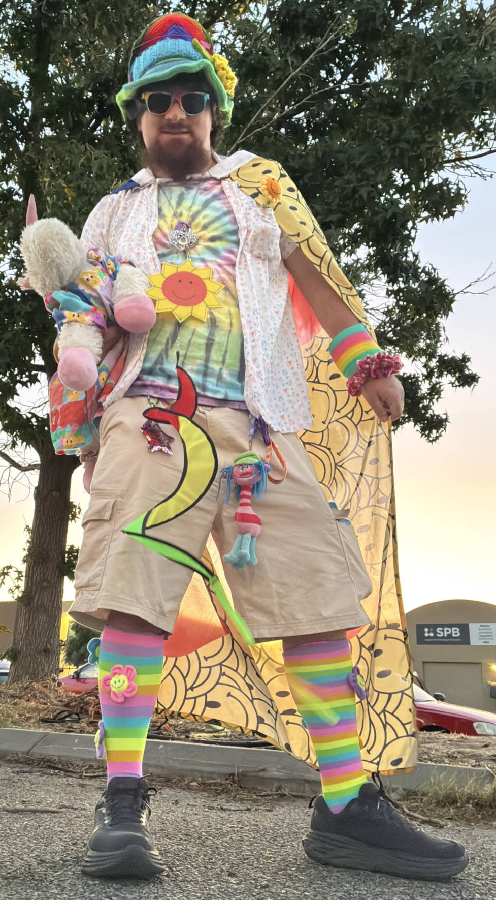Slinkyfam with unicorn plushy. Rainbow clothing, socks, hat, sunnies. Smiley face cape.