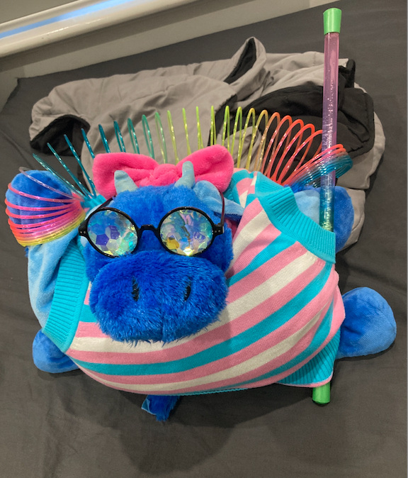Dragon plushy, slinky held in hand, holding rainbow wand in other hand, wearing sparkly glasses