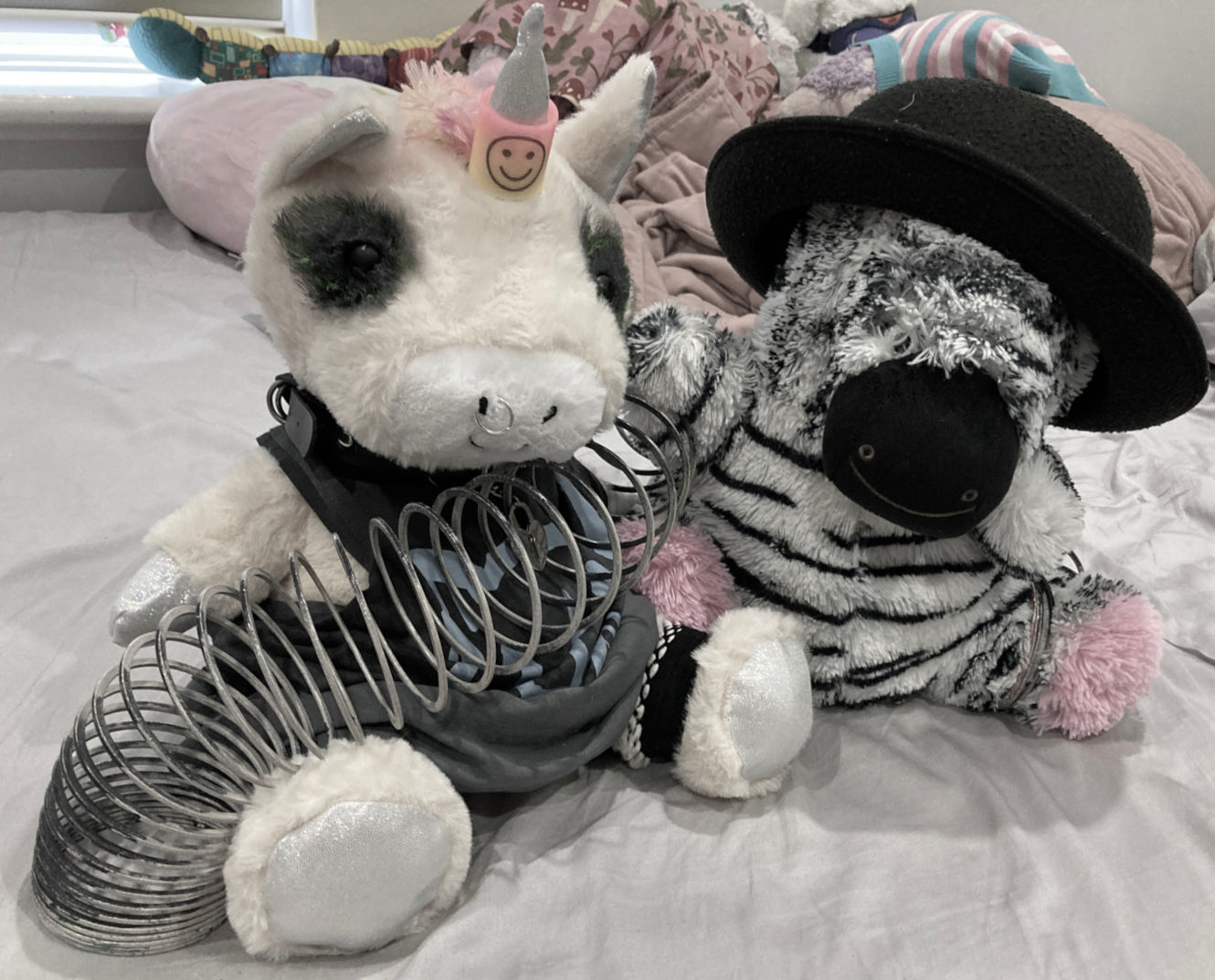 E-girl unicorn and zebra plushies playing with black and white slinky. Zebra wearing bowler hat.