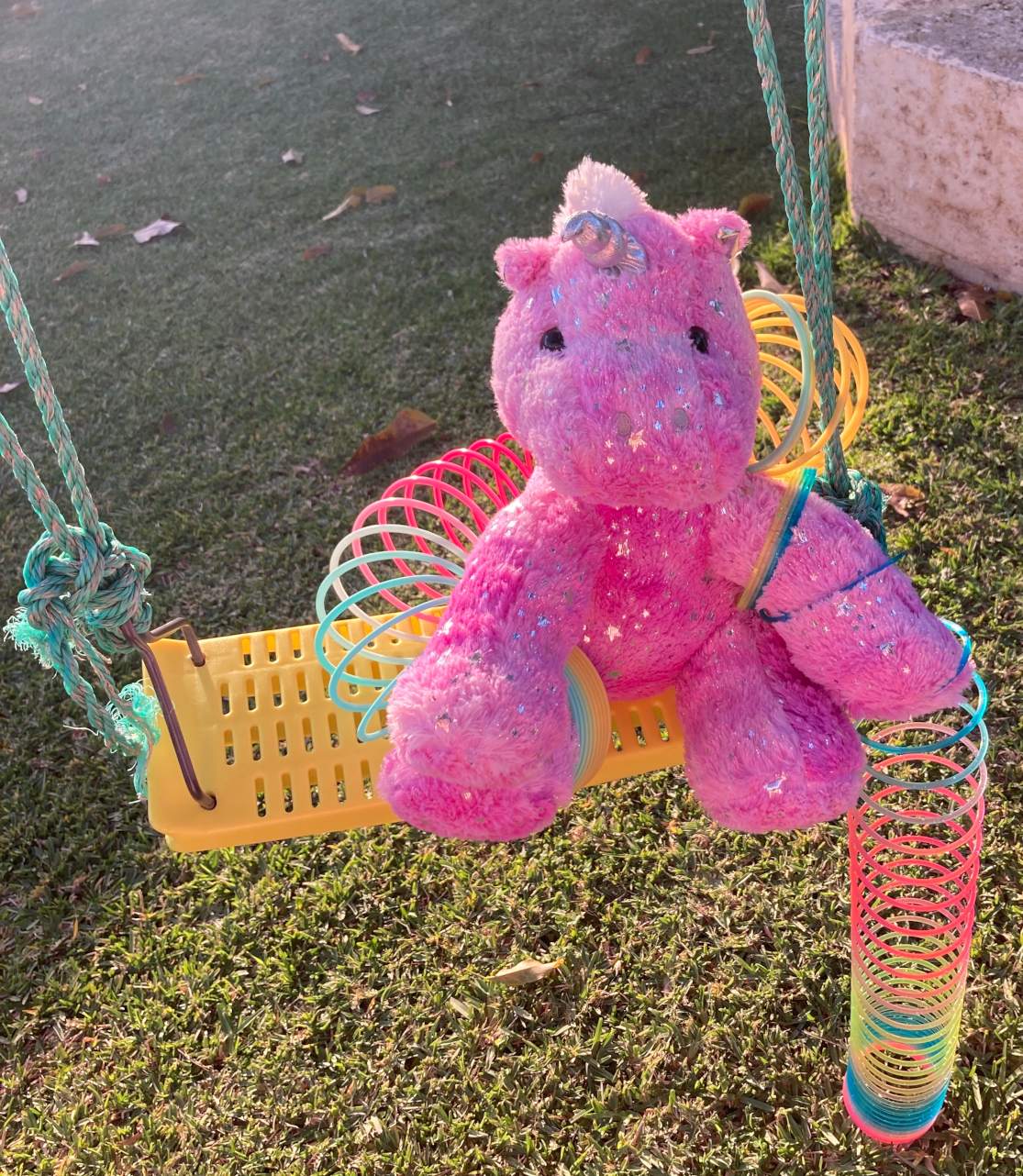Pink Unicorn sitting on swing playing with two slinkies, clear weather daytime
