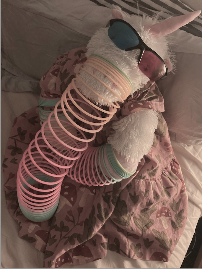 Unicorn plushy,cyan and red 3d glasses on,slinky hanging off snout, one slinky coiled around hands